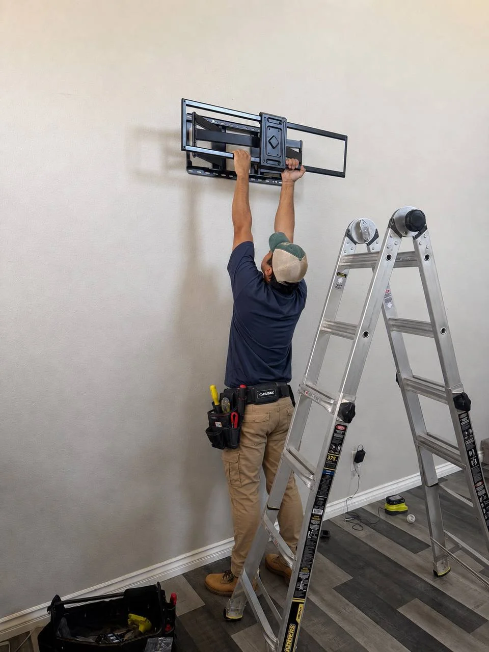 Technician mounting 100 inch TV bracket on drywall wall in Irvine CA living room